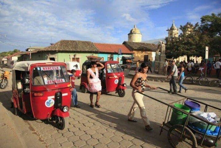 Street scene with red motorized tricycles, pedestrians, and a church in the background.
