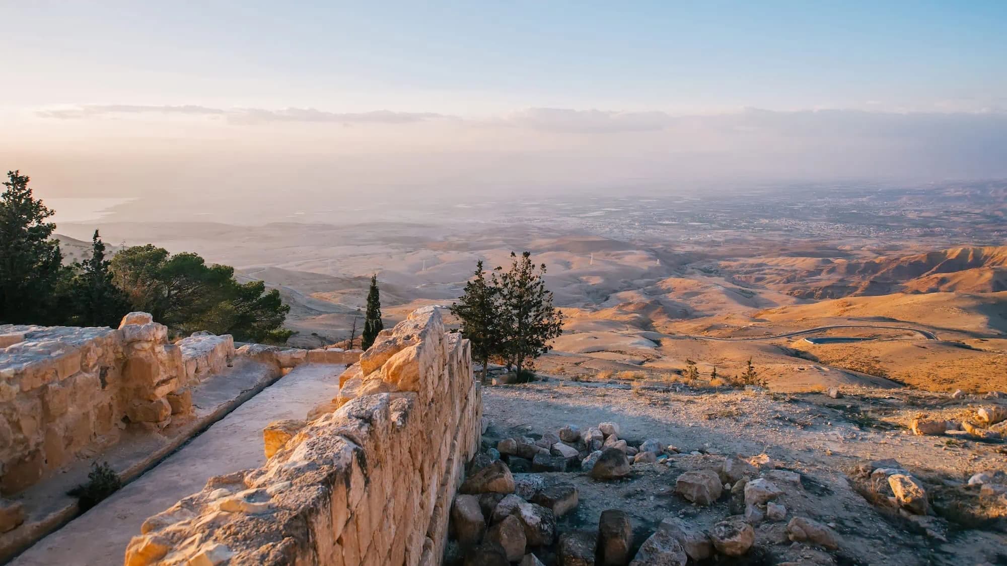 Elevated view of arid northern Jordanian hills with stone ruins in foreground, distant city, and hazy sky at golden hour