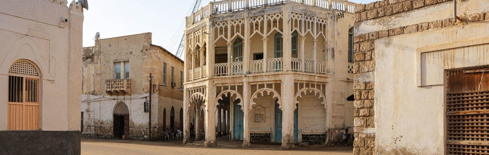Wide street view of traditional highland architecture with ornate balconies and arched colonnades in a sunlit town square in Adi Keyh, Eritrea.