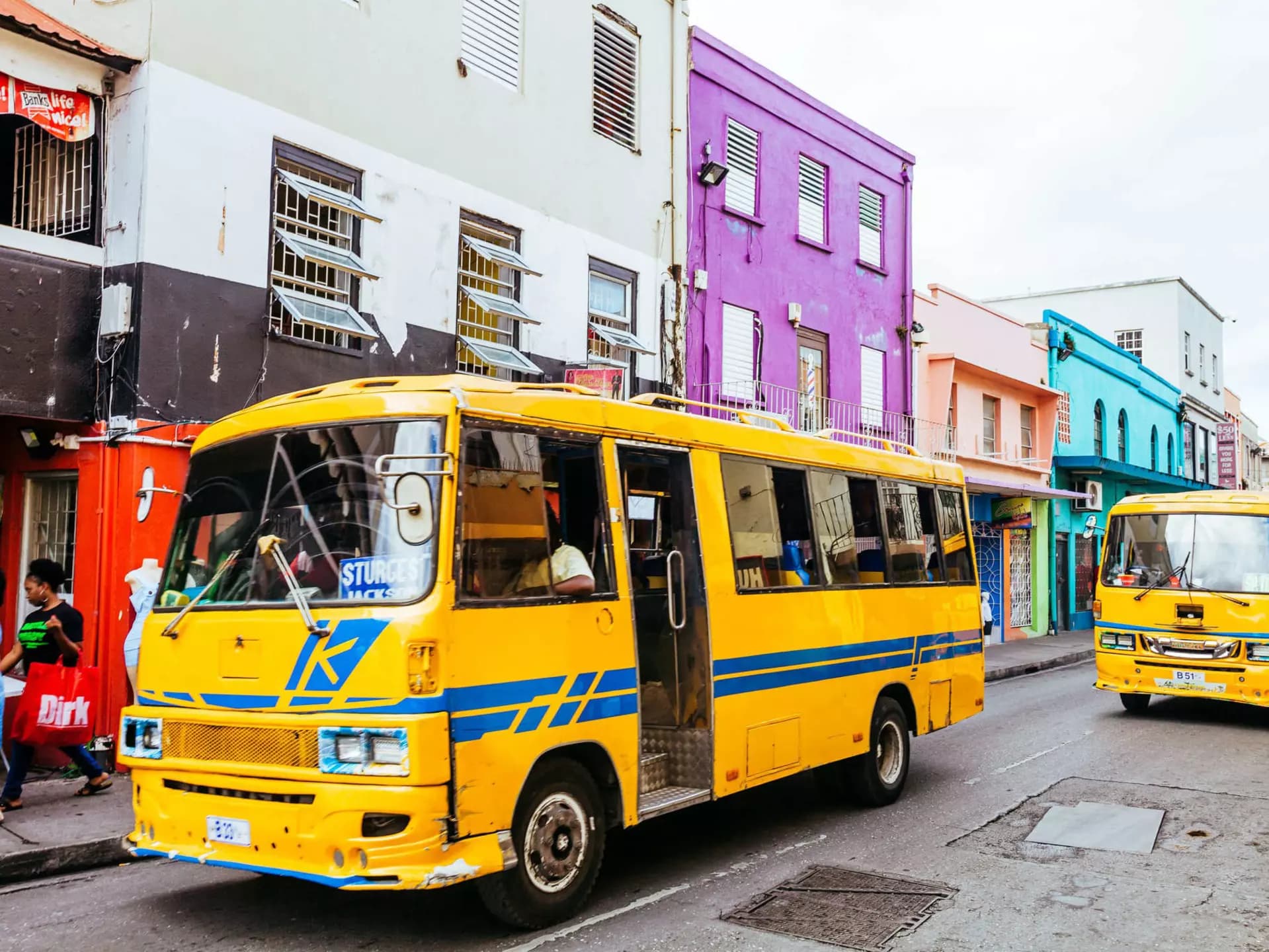 A yellow minibus taxi navigates a street lined with vibrant, colorful buildings in a Mauritian town, capturing local transit and architecture.