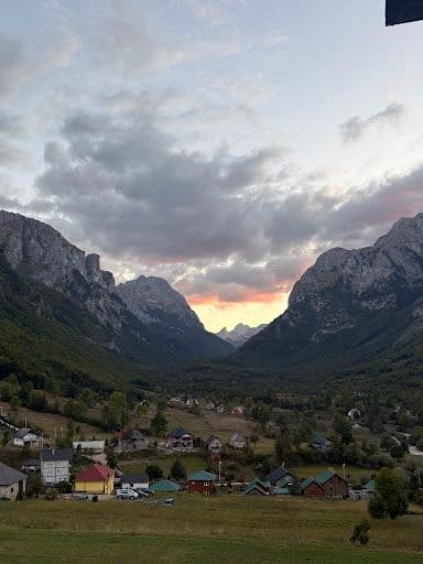 Valley landscape with village houses, forested hills, and dramatic cloudy sky at dusk.