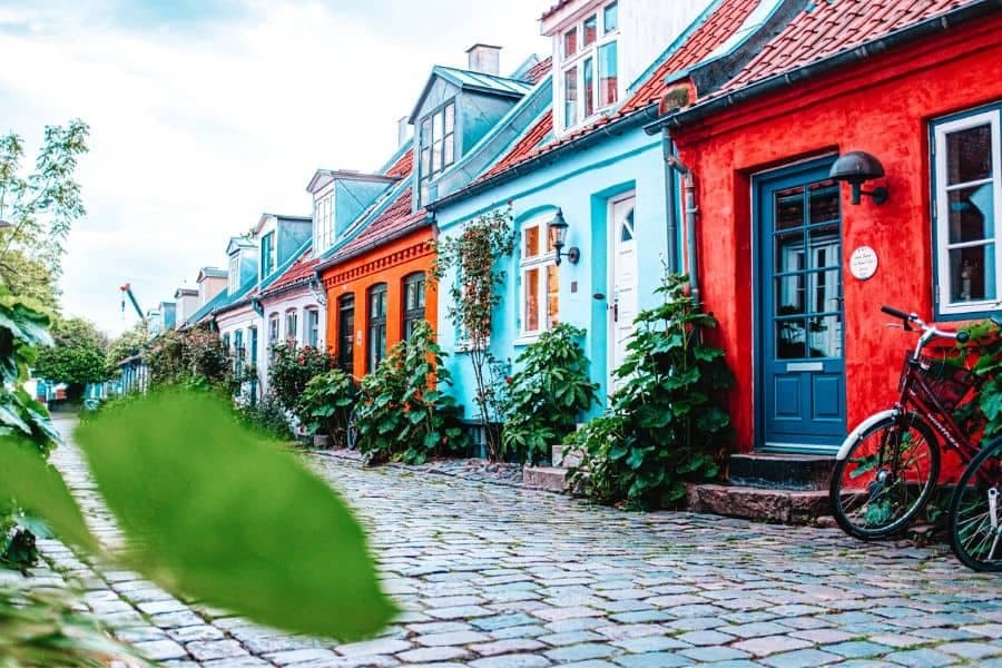 Colorful historic row houses line a cobblestone street in Præstø, featuring a red building with a blue door and a bicycle parked nearby.
