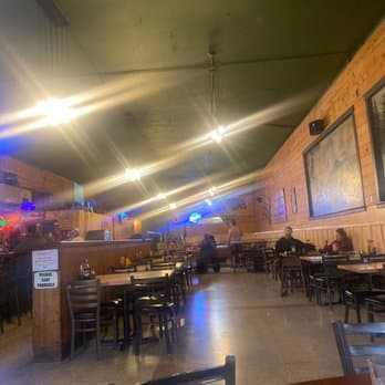 Interior view of a rustic diner with wooden walls, tables, and chairs, featuring overhead lighting and patrons seated in the background.