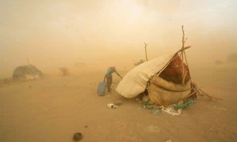 Dusty desert landscape with a makeshift shelter and hazy, sand-filled air in Sudan's River Nile State.