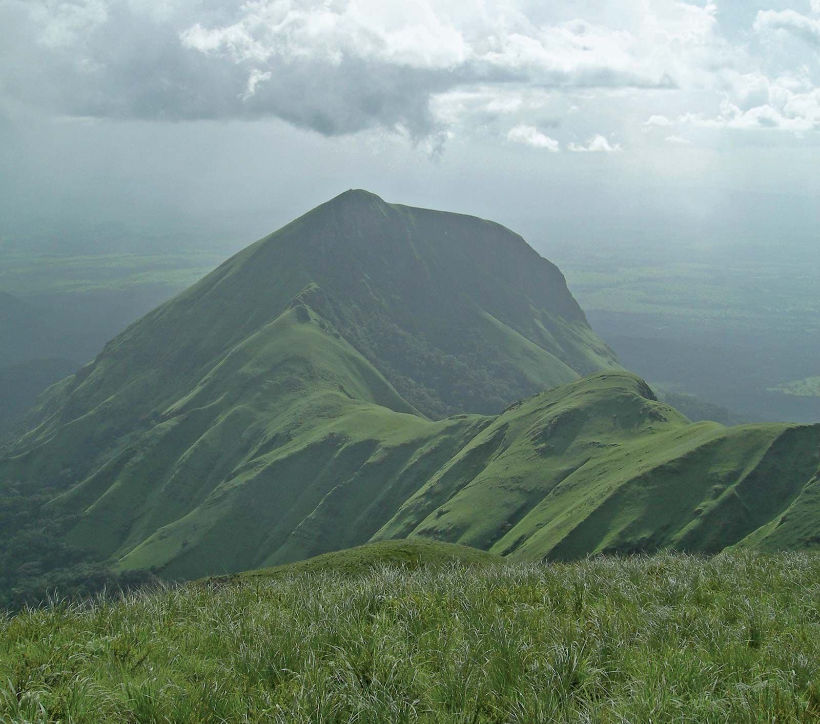 Lush green mountain slopes and grassy foreground under a cloudy sky in the Guinea Highlands