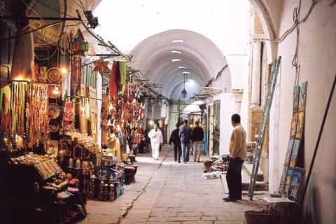 Narrow alley in the Hammam Sousse medina with traditional buildings, shopfronts, and market goods on display