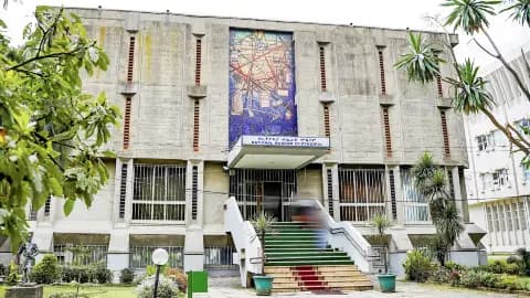 Exterior of a concrete church building with a large mosaic above the entrance, green stairs, and surrounding tropical plants.