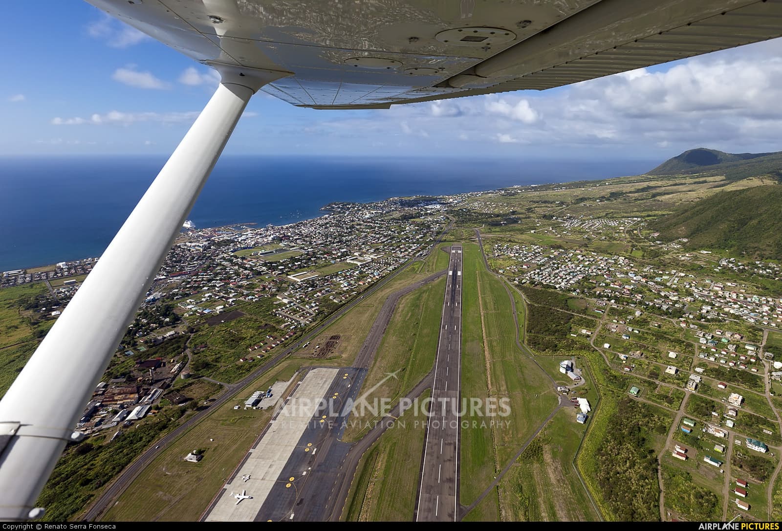 Aerial view of Robert L. Bradshaw International Airport (SKB) in Cotton Ground, Saint Kitts and Nevis, showing the terminal and runway against green hills.