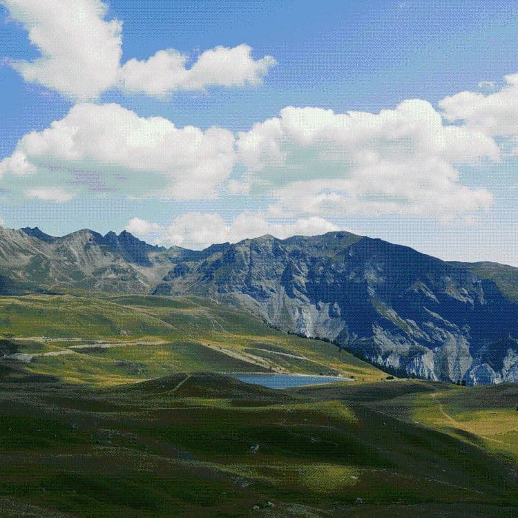 Wide landscape of the rolling hills and small lake in the Bulqizë valley under a partly cloudy sky.