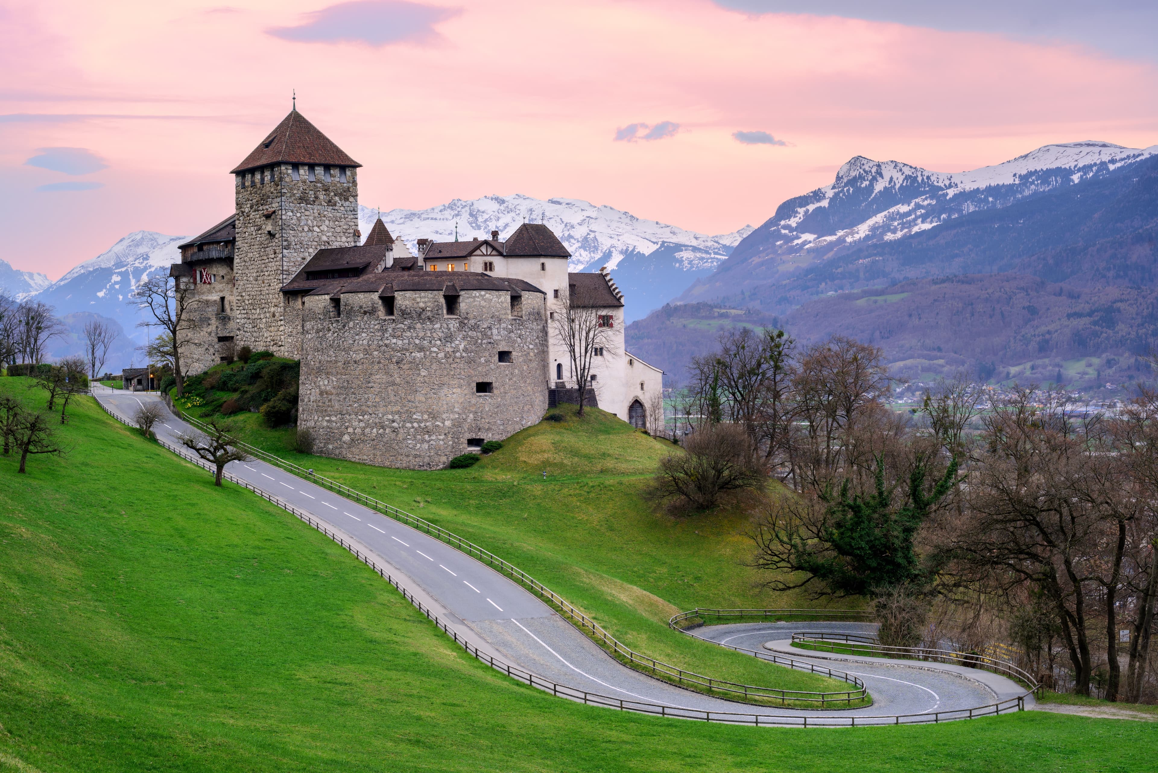 Establishing shot of Vaduz Castle, a historic fortress in Liechtenstein, viewed from below with green valley and mountains in background