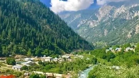 Aerial view of a small town nestled in a green mountain valley with a river, in the Paktika region near Zaṟah Sharan.