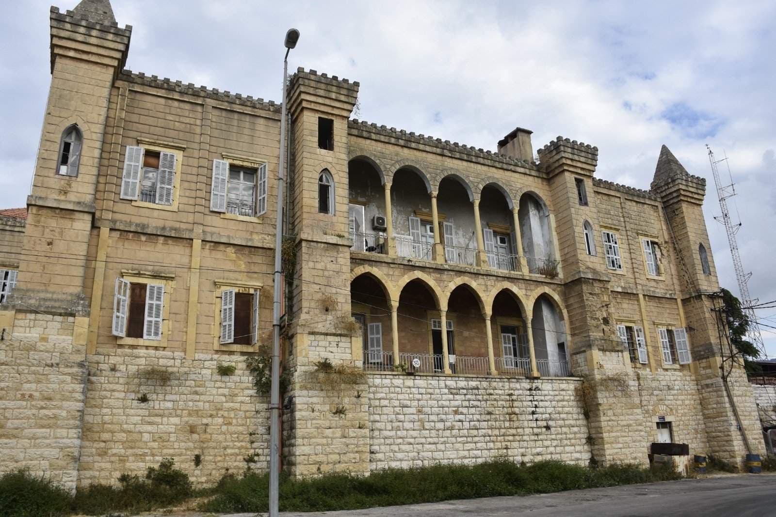Exterior of a historic stone mansion in Baabda with crenellated towers, arched loggias, and shuttered windows.