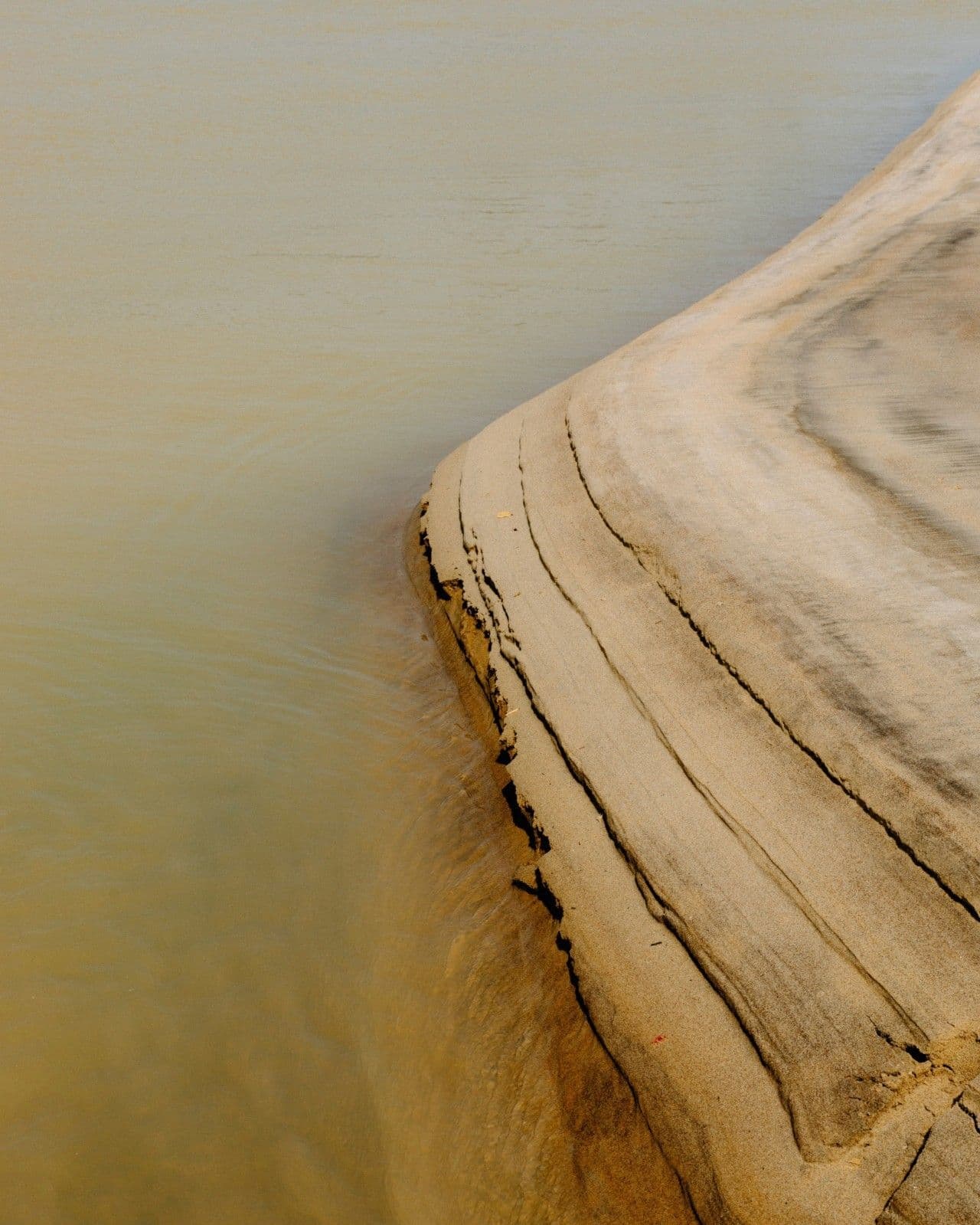 Close-up of a smooth, weathered rock formation meeting calm, murky water in Ghana