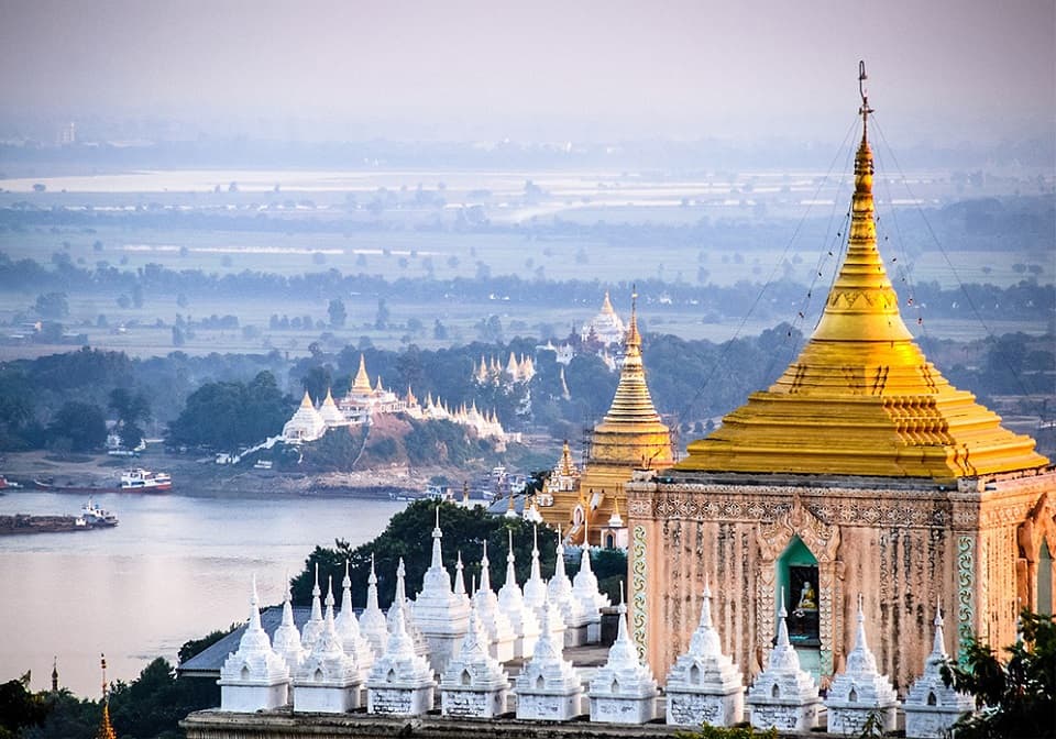 Golden pagodas and white stupas overlook the Irrawaddy River and distant plains from a high vantage point on Mandalay Hill.