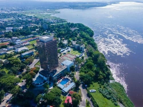 Aerial view of a tall hotel building with a pool situated on a lush green riverbank in Bolobo.
