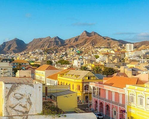 Colorful colonial buildings and streetscape in Porto Novo, Cape Verde, set against arid mountains under a clear blue sky.