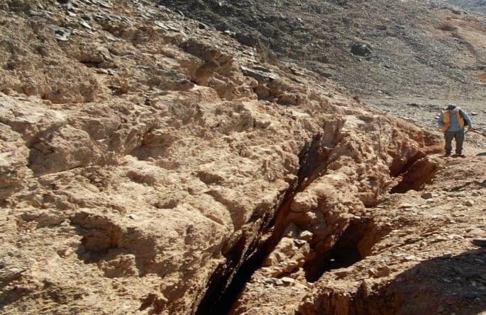 Rocky desert terrain with a dry riverbed and a hiker walking along the slope.