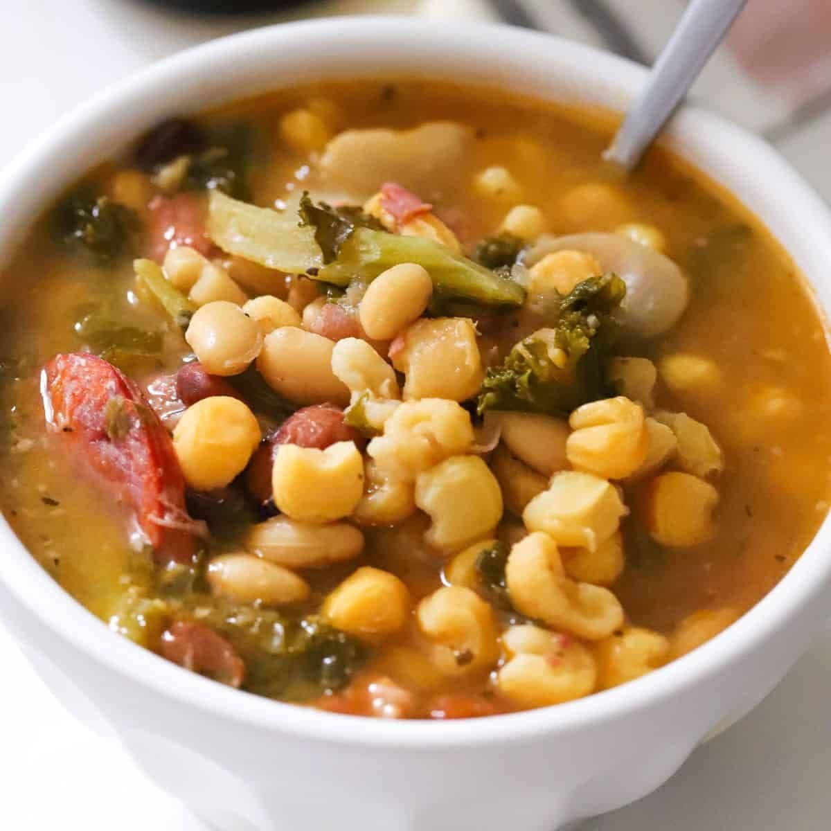 Close-up shot of a white bowl filled with hearty cachupa stew containing corn, beans, greens, and meat.