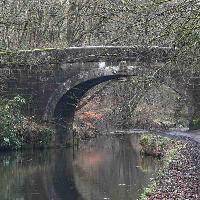 Stone arch bridge over a calm river in Yarrow Valley Country Park near Euxton, with bare trees and a leaf-strewn bank in late autumn.