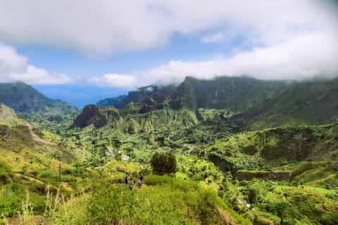Scenic landscape of lush green mountains and valleys in Santo Antão, Cape Verde, featuring winding roads and distant ocean views under cloudy skies.