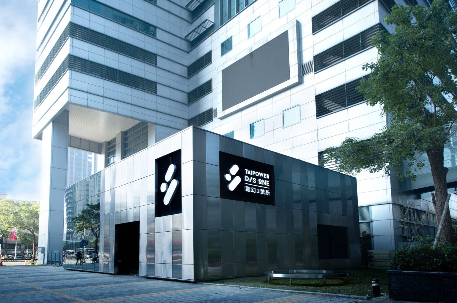 Exterior of a sleek modern venue in central Banqiao, featuring a metallic kiosk with Taipower D/S ONE branding and a large white building behind.