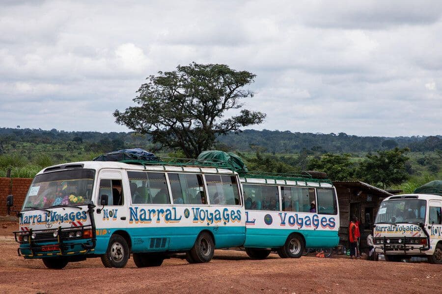 Two white and blue minibuses with 'Narral Voyages' lettering parked on a dirt road in a rural landscape.