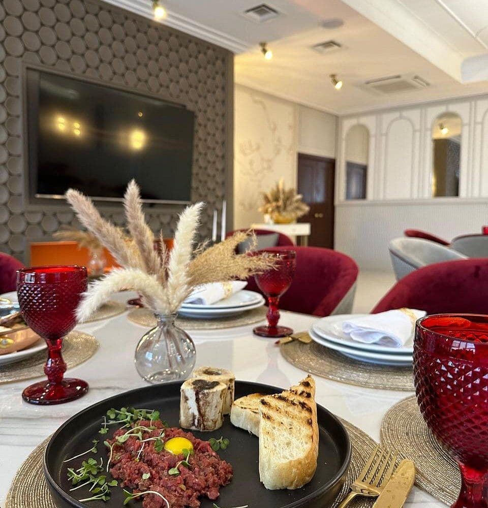Interior dining scene with a set table, red glassware, pampas grass centerpiece, and a plated dish at a resort in Tula Oblast near Tonshalovo.