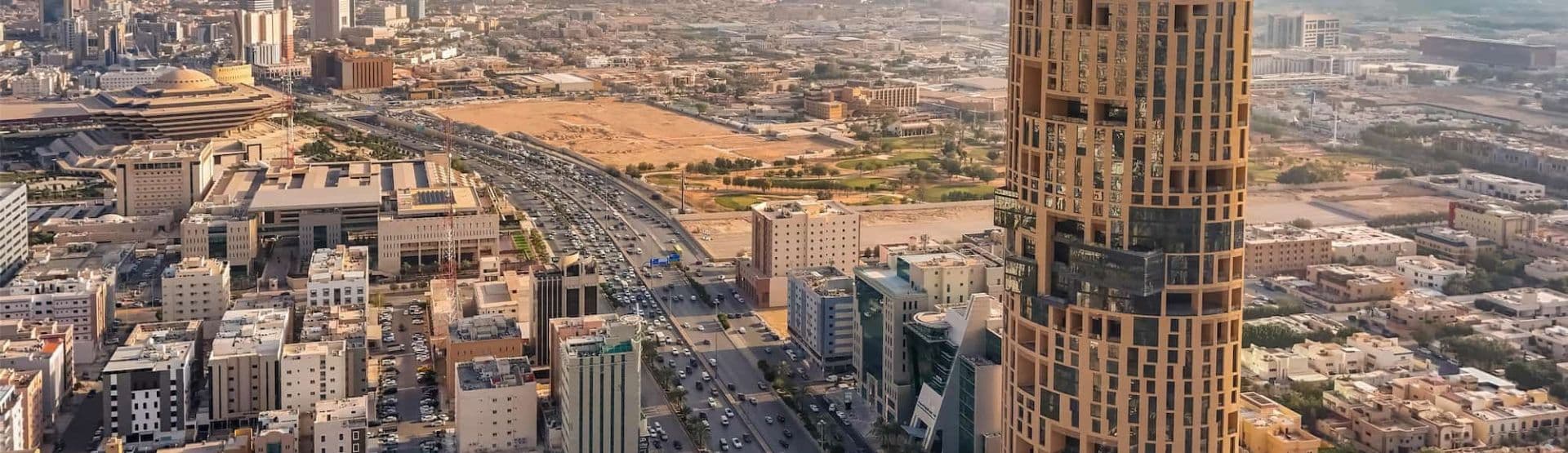 Aerial view of Kuwait City skyline with a prominent skyscraper, highway, and urban buildings.