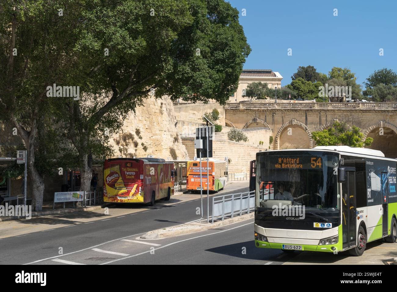 Public transportation buses parked at a bus stop adjacent to historic stone walls in Malta