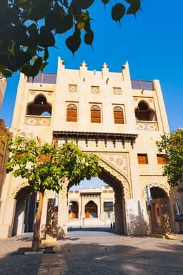 Exterior of a historic sandstone market building with arched entryways and decorative crenellations under a clear blue sky.