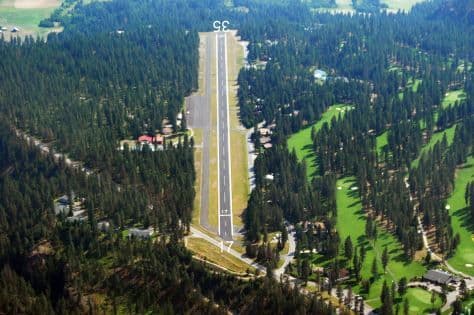 Aerial view of Chewelah Municipal Runway in a dense pine forest with scattered buildings and green fields.