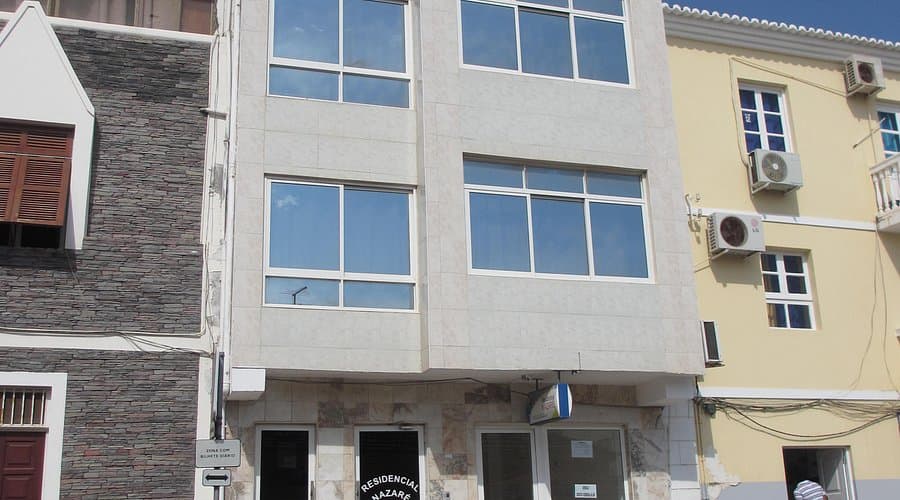 Street-level view of a beige building facade with large windows and a sign reading Residencial Nazare, flanked by stone and yellow buildings.