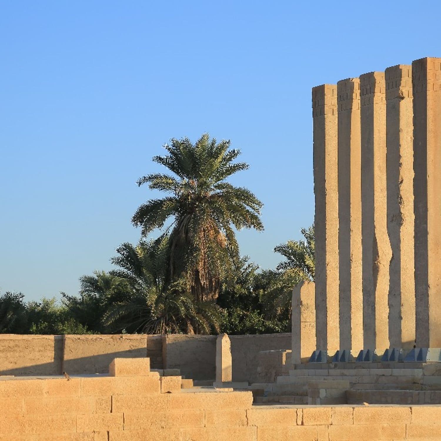 Weathered sandstone ruins with tall columns and a palm tree under a clear blue sky, evoking the historical stone structures of Kamaran.