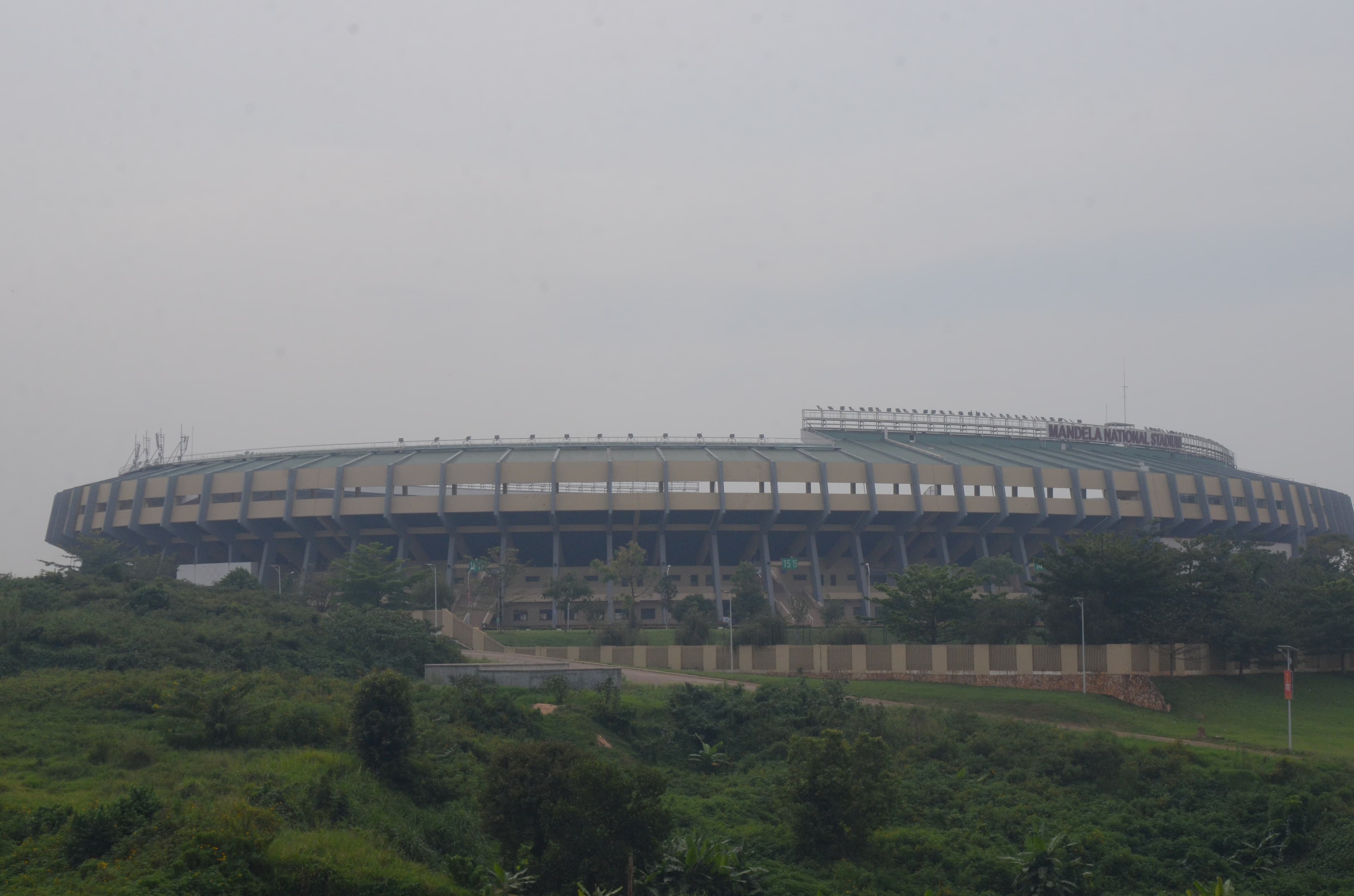 Exterior view of the Mandela National Stadium in Bweyogerere, featuring its distinctive circular architecture and surrounding green landscape under an overcast