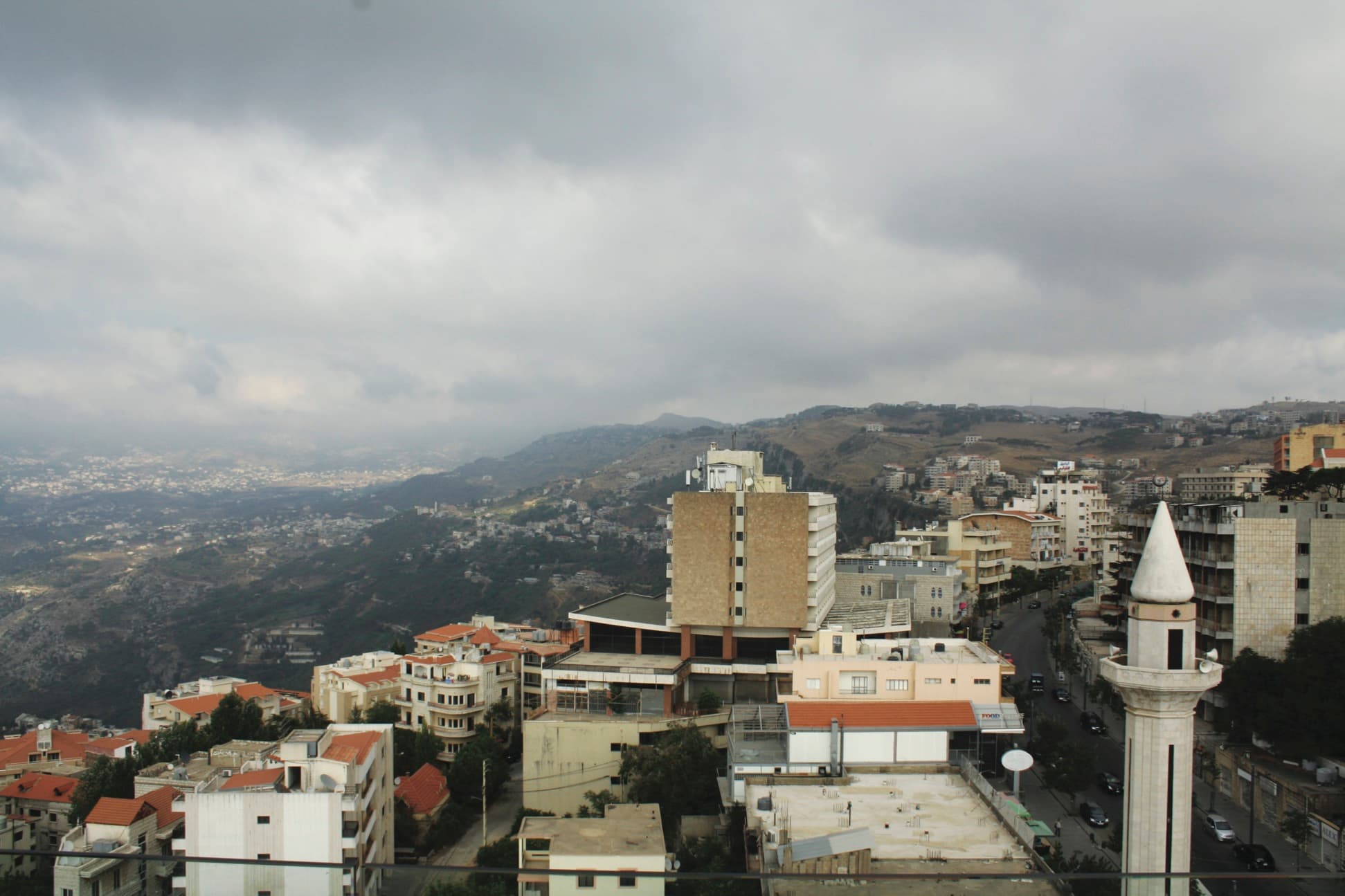 Overcast panoramic view of Bhamdoun featuring a prominent minaret, dense hillside architecture, and a winding road through the town.