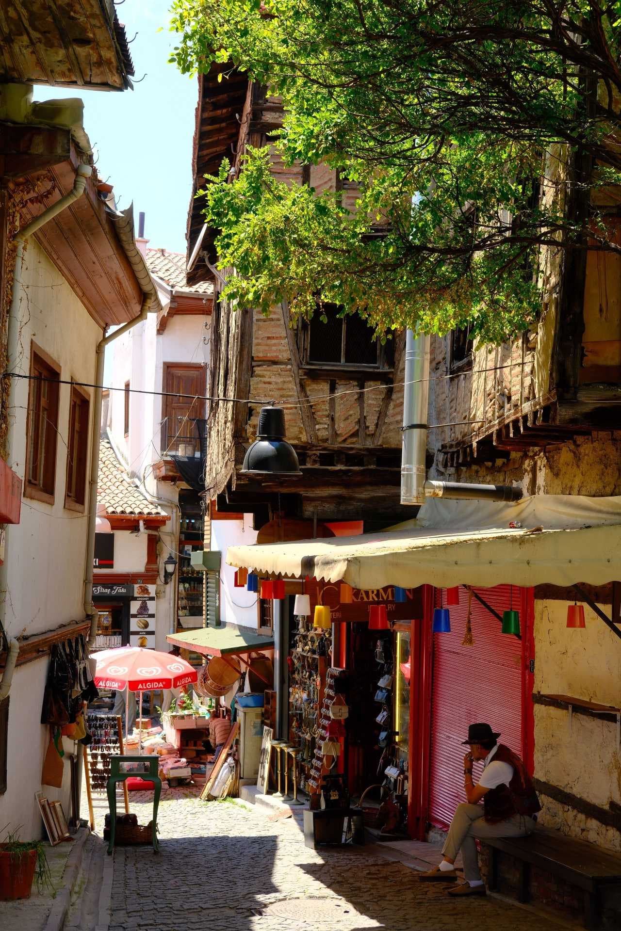 Narrow cobblestone street in Ohrid old town with souvenir shops, market stalls, and a seated man.