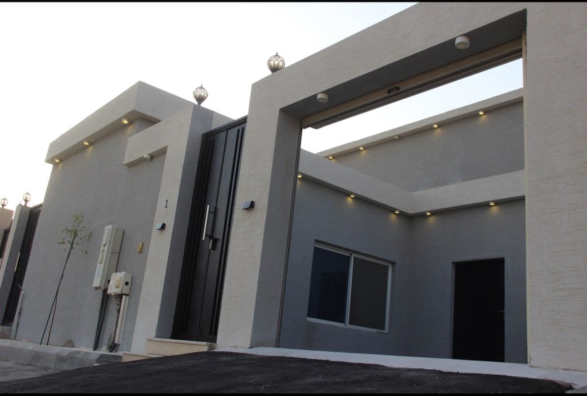 Exterior of a modern, minimalist apartment building with grey and white walls, dark doors, and recessed lighting.