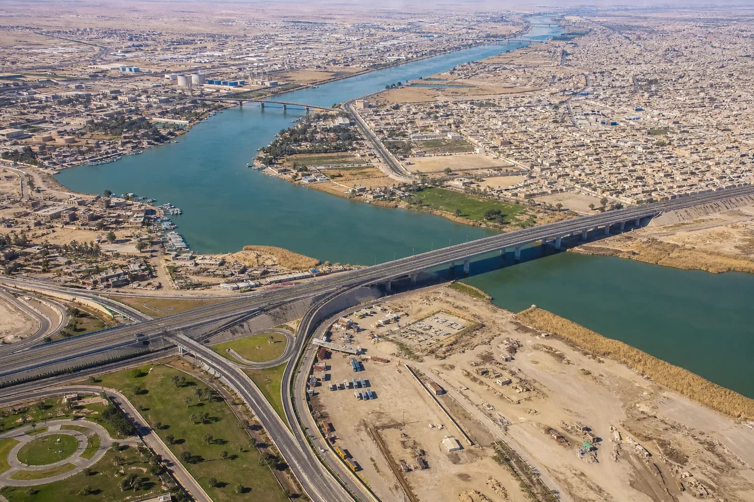 Aerial daytime view of the Tigris River at Mosul with bridges, highways, and dense urban development on both banks.