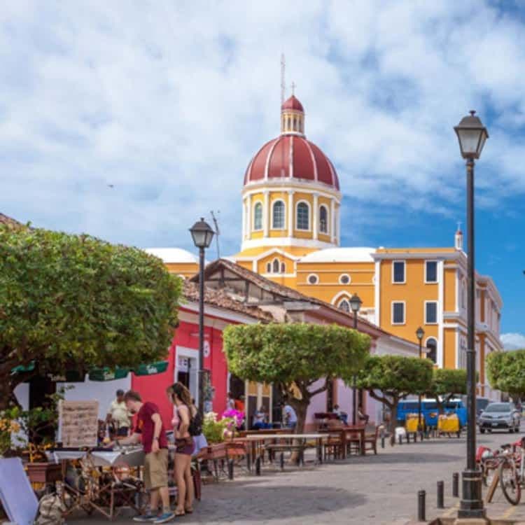 Colonial plaza with a yellow and red-domed church, colorful buildings, street vendors, and pedestrians under a blue sky.