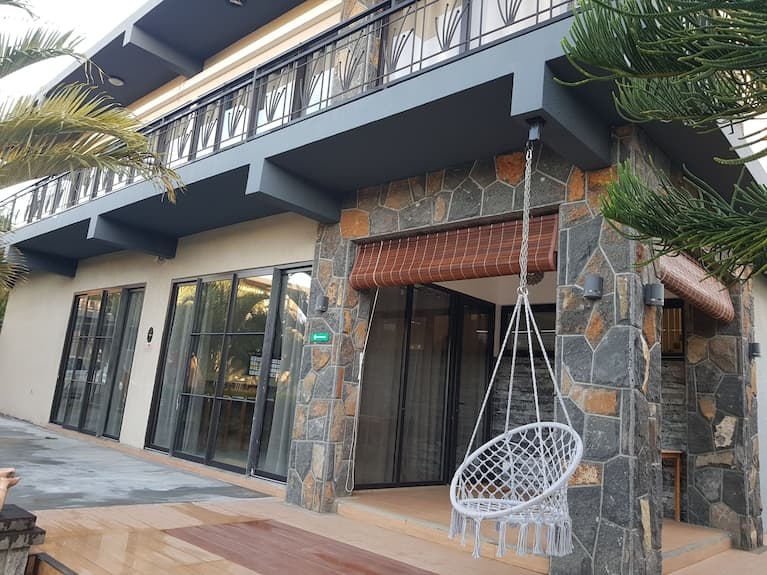 Exterior view of a modern two-story building in Fond du Sac featuring stone cladding, a balcony, and a hanging white macrame chair on a wooden deck.