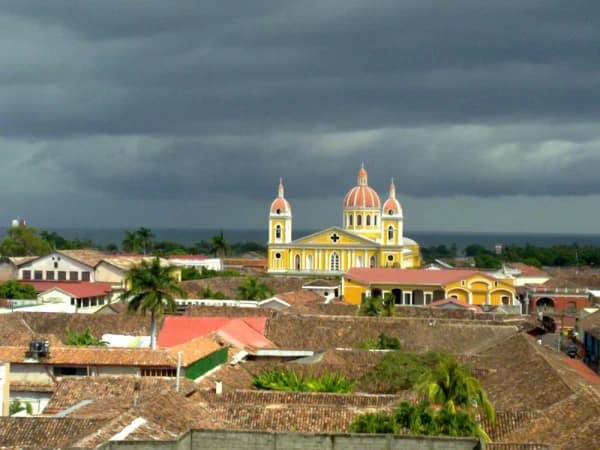 Aerial view of Diriomo town featuring a prominent yellow church with red domes, surrounded by terracotta rooftops under a dramatic cloudy sky.