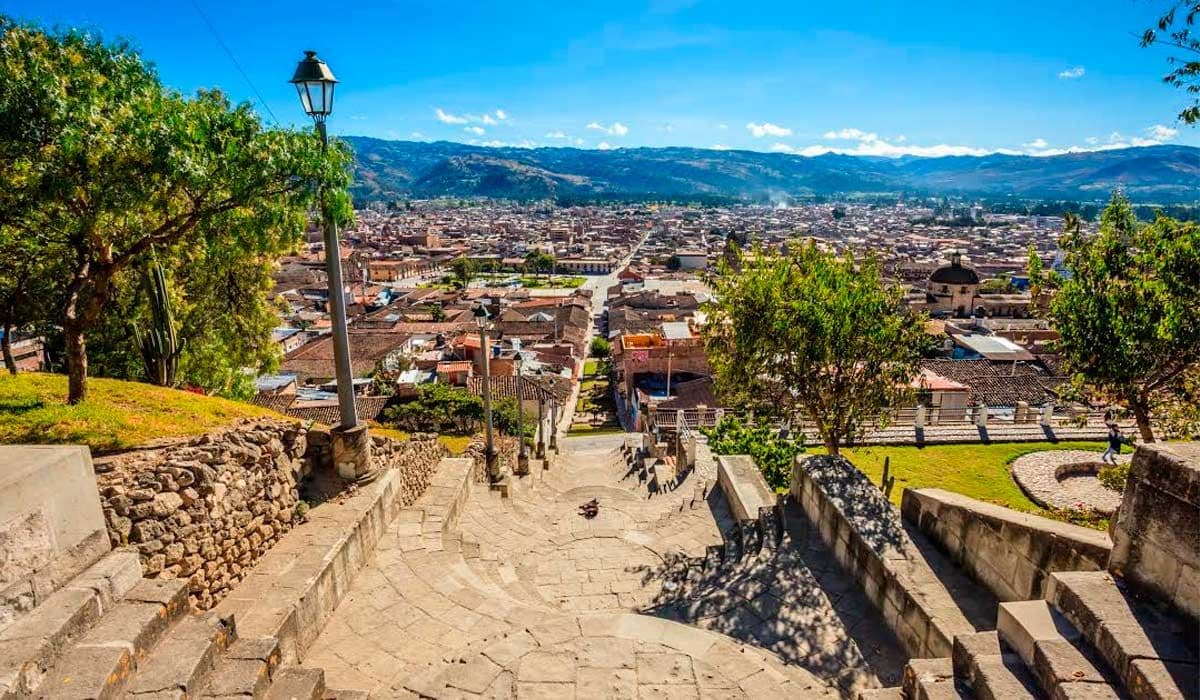 Elevated stone staircase overlooks a dense Honduran highland town with red roofs, distant mountains, and a clear blue sky.