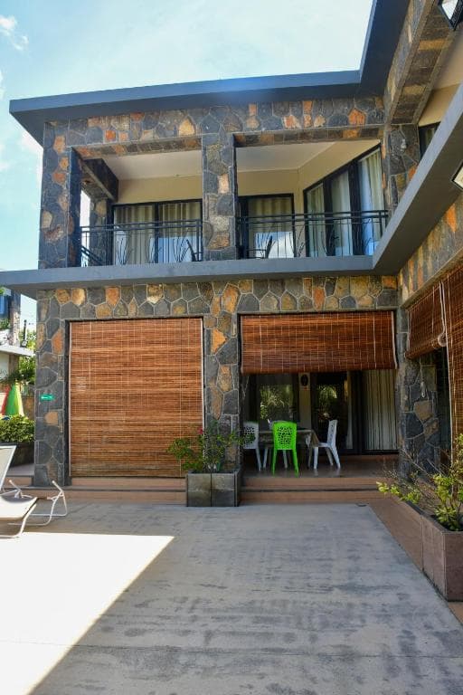 Modern two-story building facade featuring stone cladding, bamboo blinds, and a patio with a green chair in Fond du Sac.
