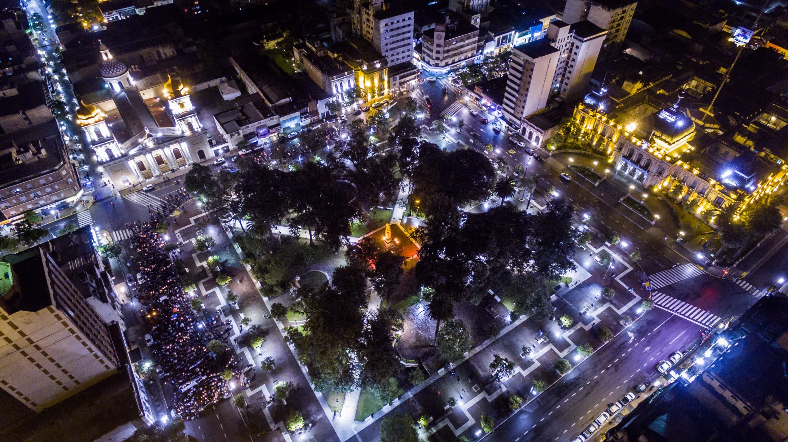 Aerial night view of Plaza Independencia in San Miguel de Tucumán showing illuminated historic buildings and the central square.