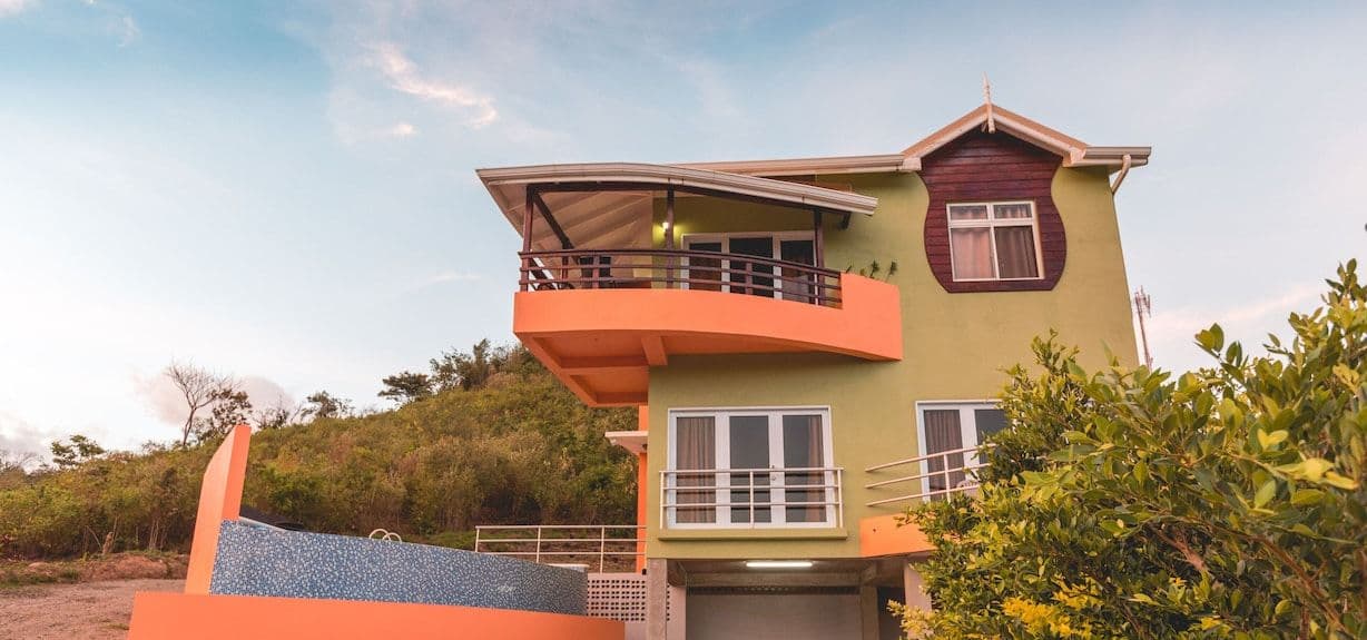Exterior view of the Marigot Hot Springs facility in Martinique, featuring a lime-green and orange building with a blue-tiled pool structure against a lush hillside.