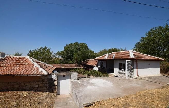 Exterior of a rural house in Tsenovo, Bulgaria, surrounded by greenery and open fields