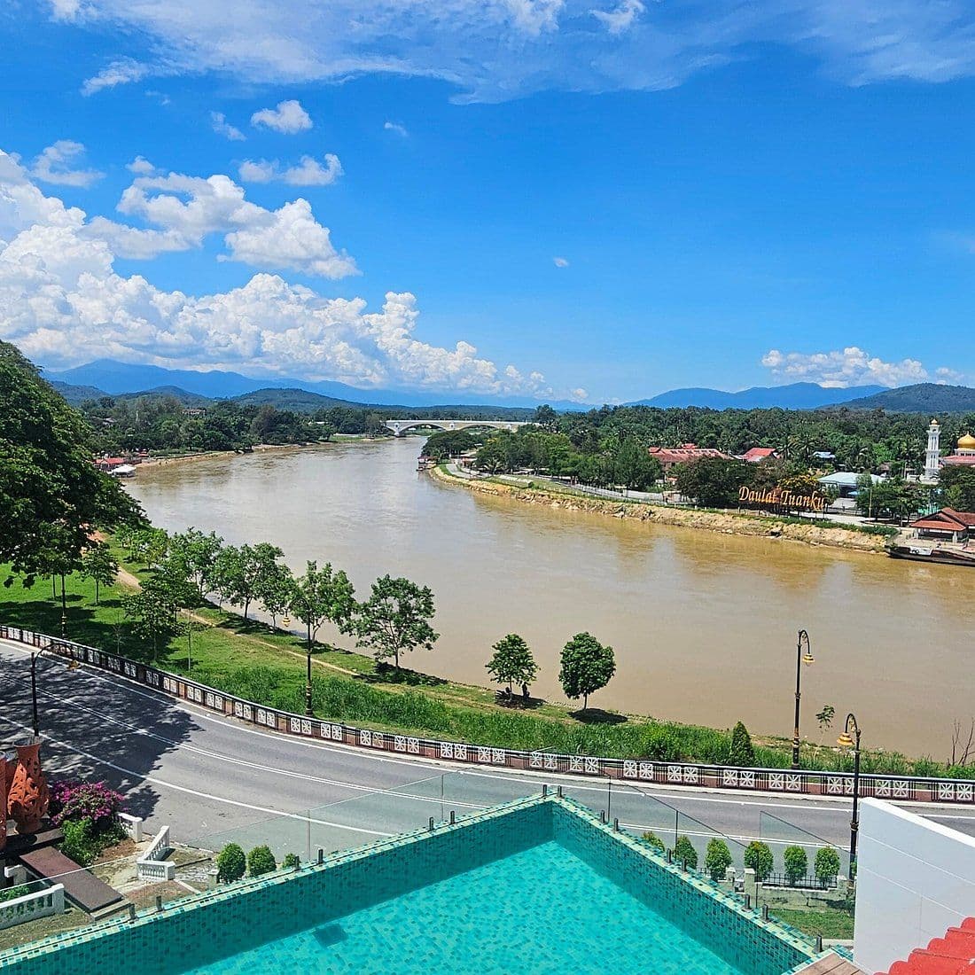 Elevated view of the Perak River flowing through Kuala Kangsar, with a bridge, town buildings, and a foreground pool