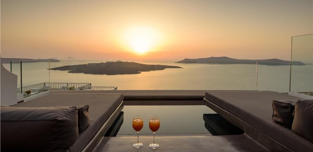 Luxury terrace with plunge pool and cocktails overlooking the Santorini caldera at sunset, featuring volcanic islands in the distance.
