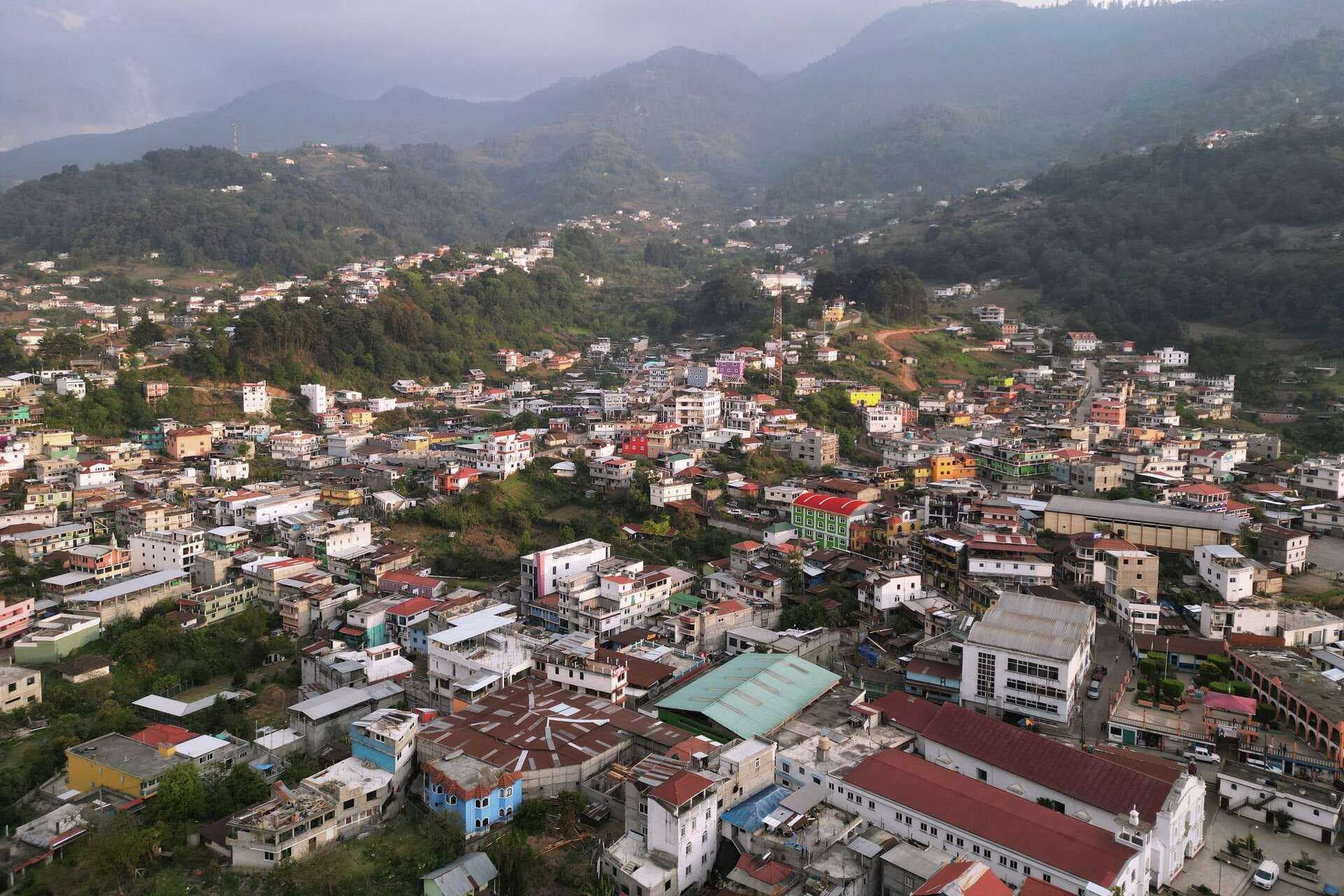 Aerial view of a densely built town nestled in a lush, mountainous valley, likely in the Suchitepequez region of Guatemala.