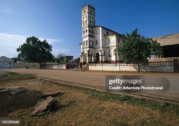 Establishing shot of the historic Catholic Church and market square in Aného, Togo, showcasing colonial architecture and local commerce